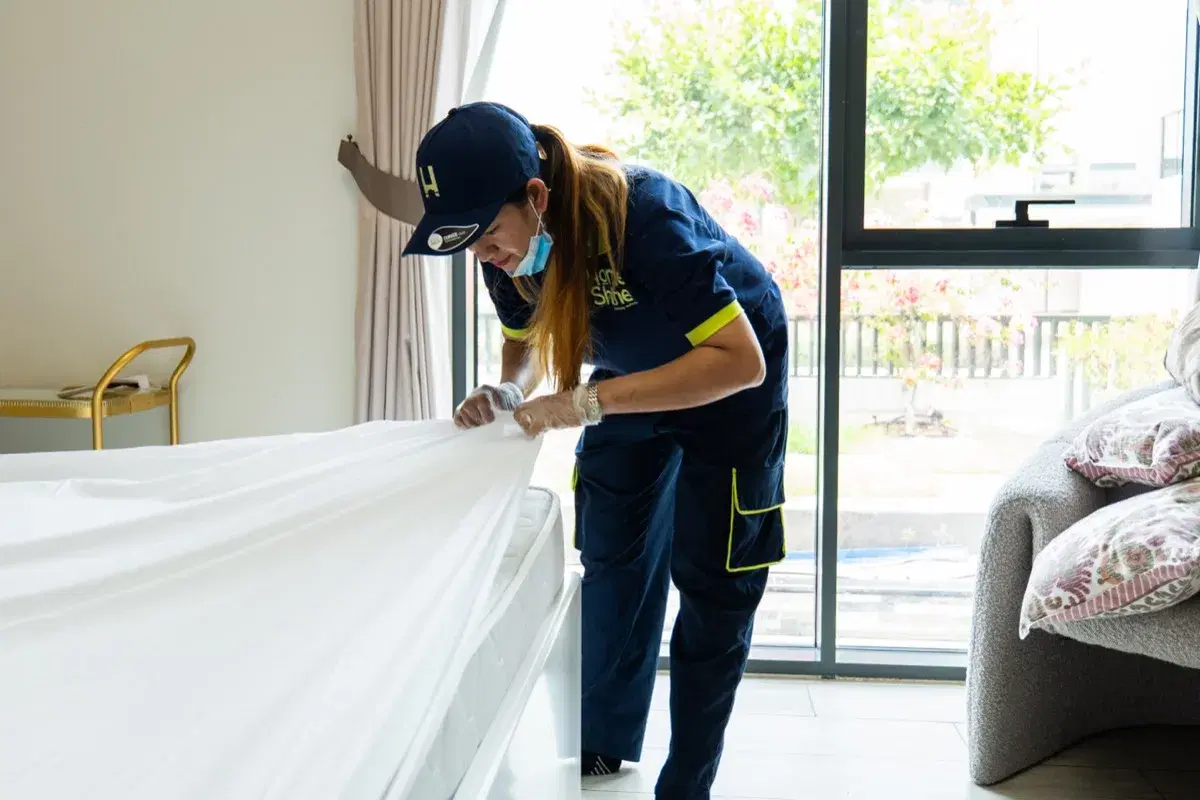 A HomeShine housekeeper spreads fresh linen during a turnover